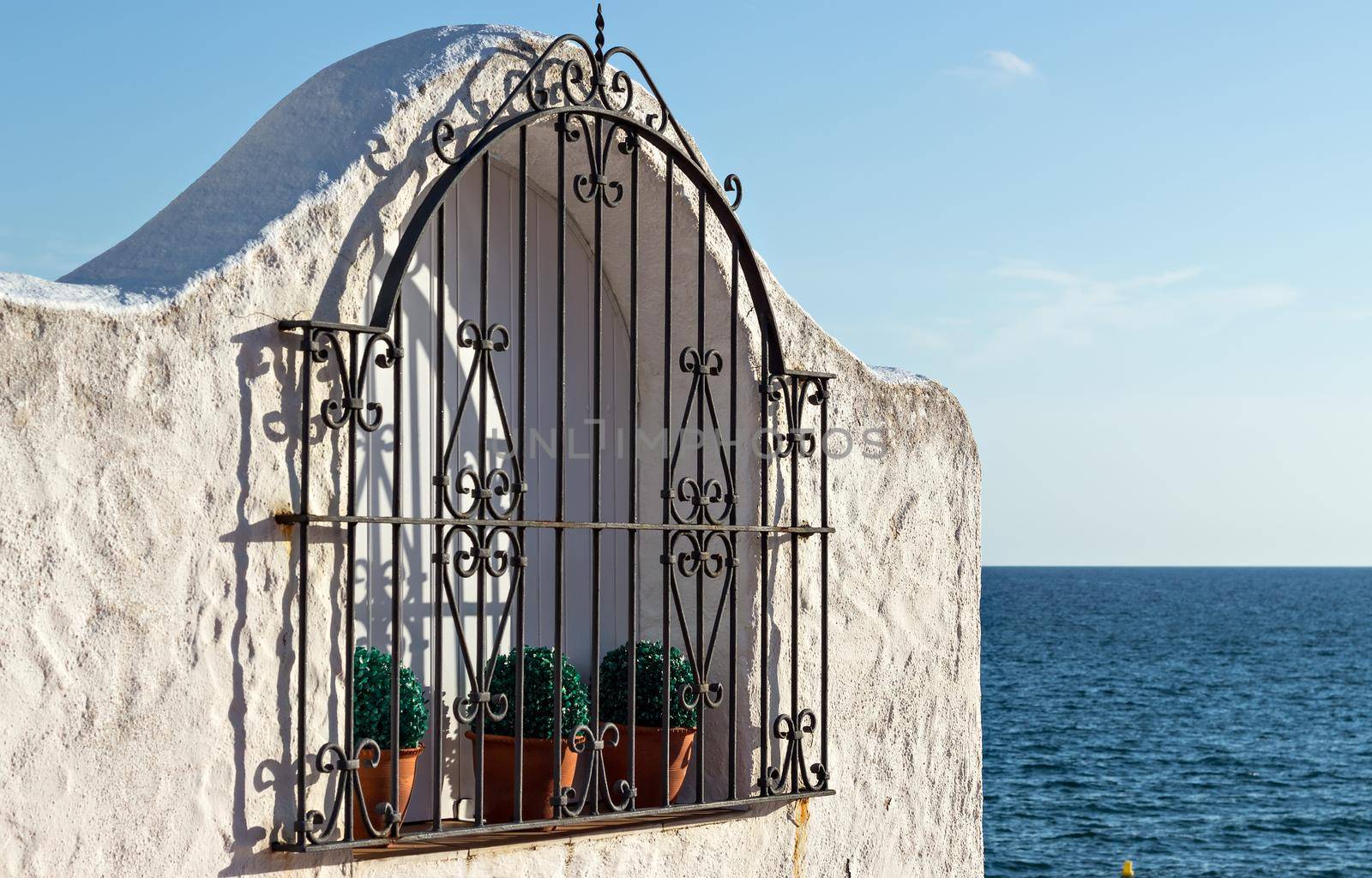 Window with pots and wrought iron fence overlooking the sea.