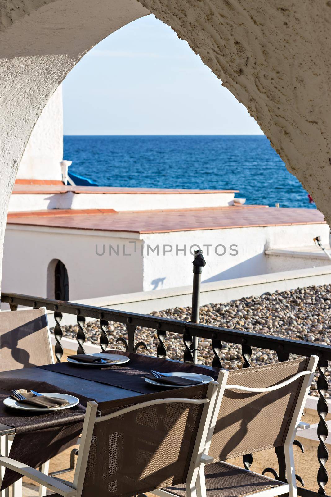 Restaurant table with plate and cutlery in front of a terrace with sea views. Holidays. Relax.