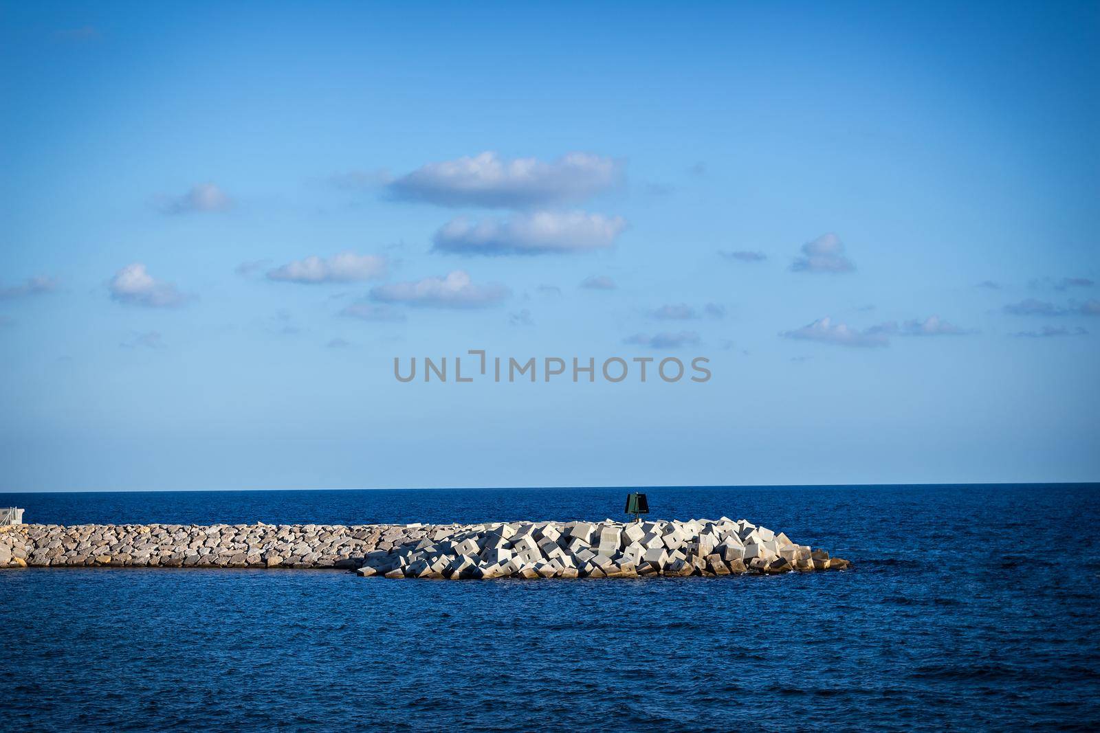 Cement groyne with calm sea and blue sky.