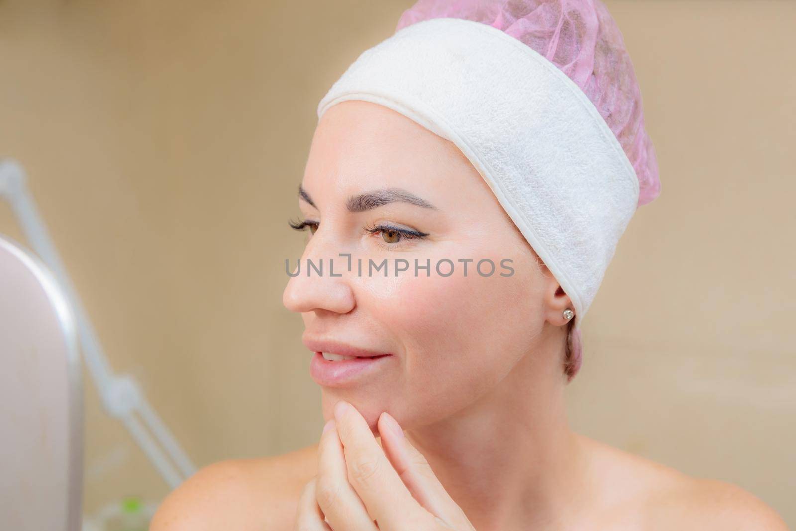 A young girl looks at her face in the mirror after a massage. Happy smile.