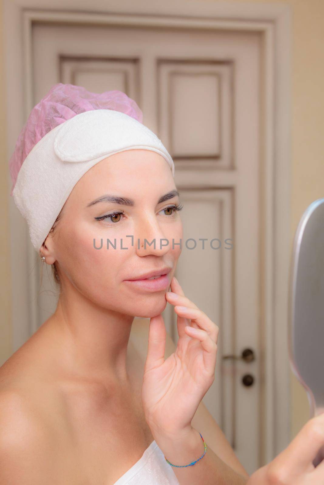A young girl looks at her face in the mirror after a massage. Happy smile.