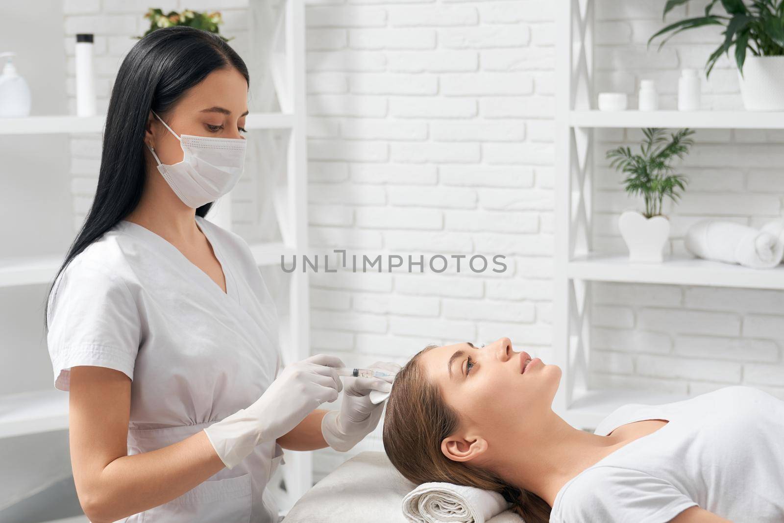 Side view of young woman on procedure for restoration condition and growth hair in professional beauty salon. Concept of improvements hair with special cosmetics.