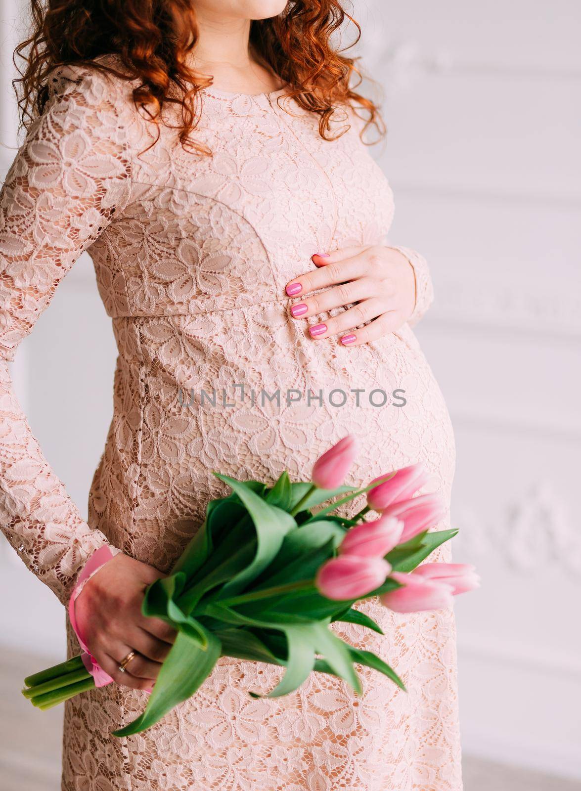 Belly of a pregnant girl and tulips in hands by Nadtochiy