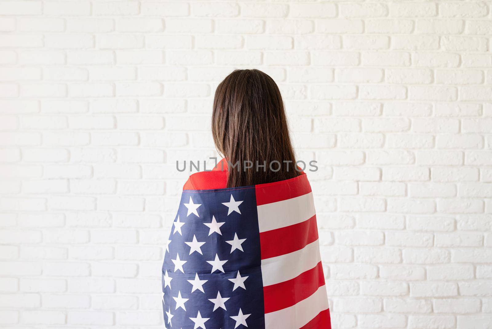 Independence day of the USA. Happy July 4th. Young smiling woman with national flag of the USA, rear view