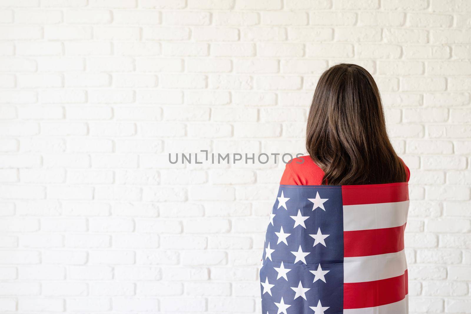 Independence day of the USA. Happy July 4th. Young smiling woman with national flag of the USA, rear view