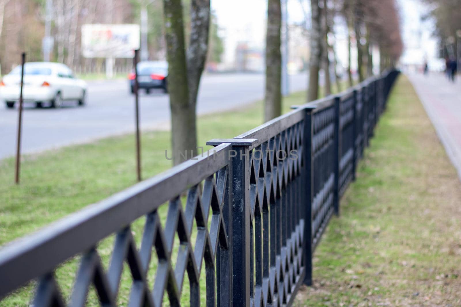 Black metal forged fence along the road with cars close-up