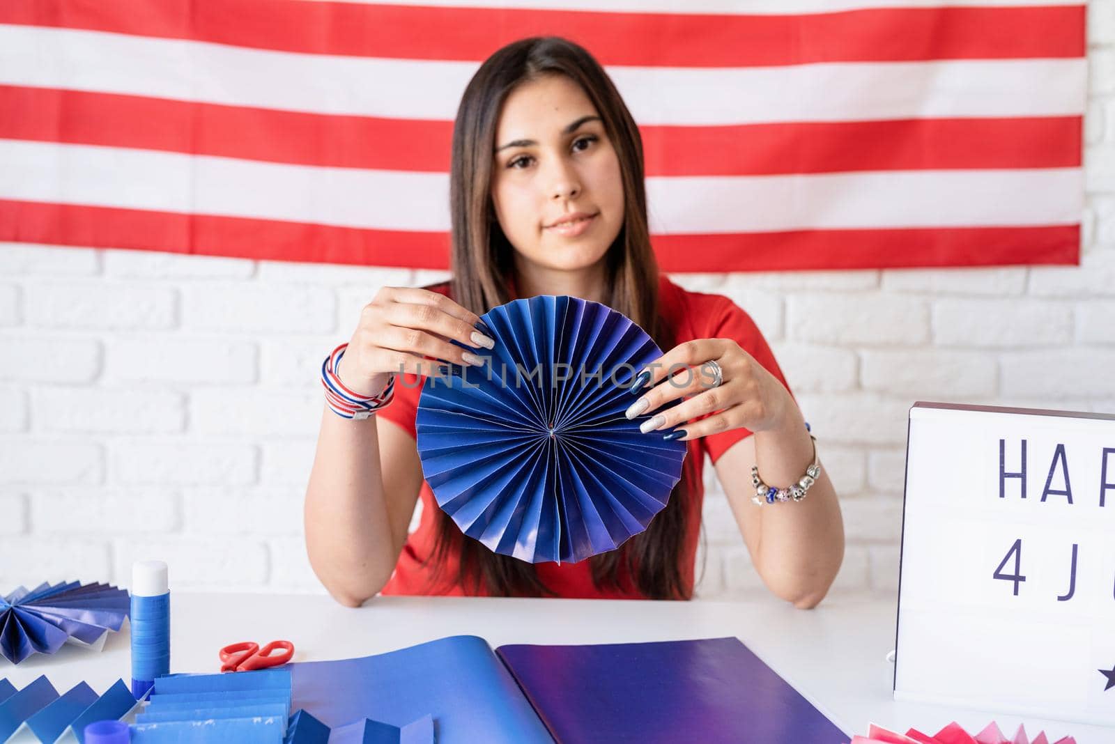 Independence day of the USA. Happy July 4th. Beautiful woman making DIY paper fans of red and blue colors to celebrate July 4th. Happy 4 July the text on the lightbox