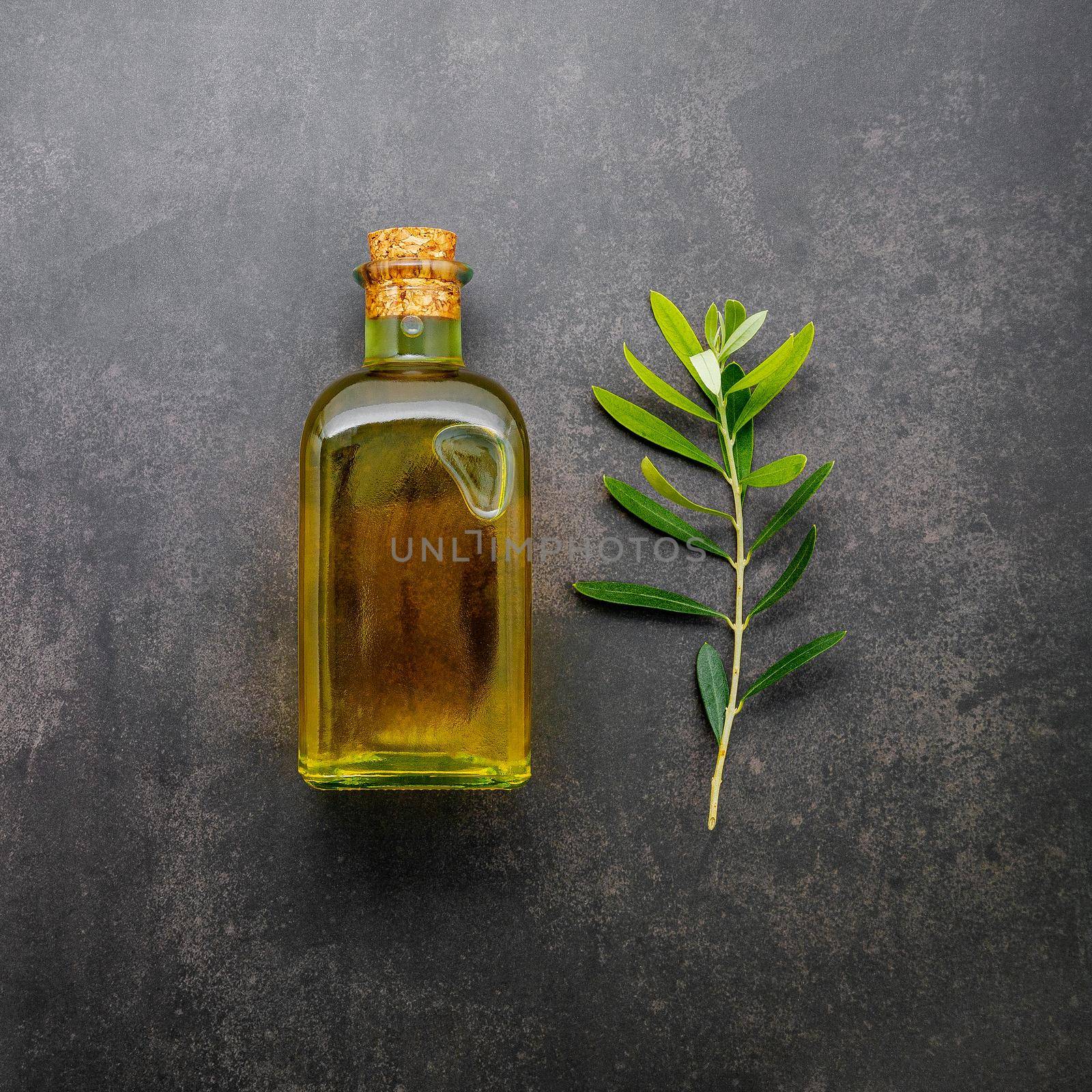 Glass bottle of olive oil and olive branch set up on dark concrete background.