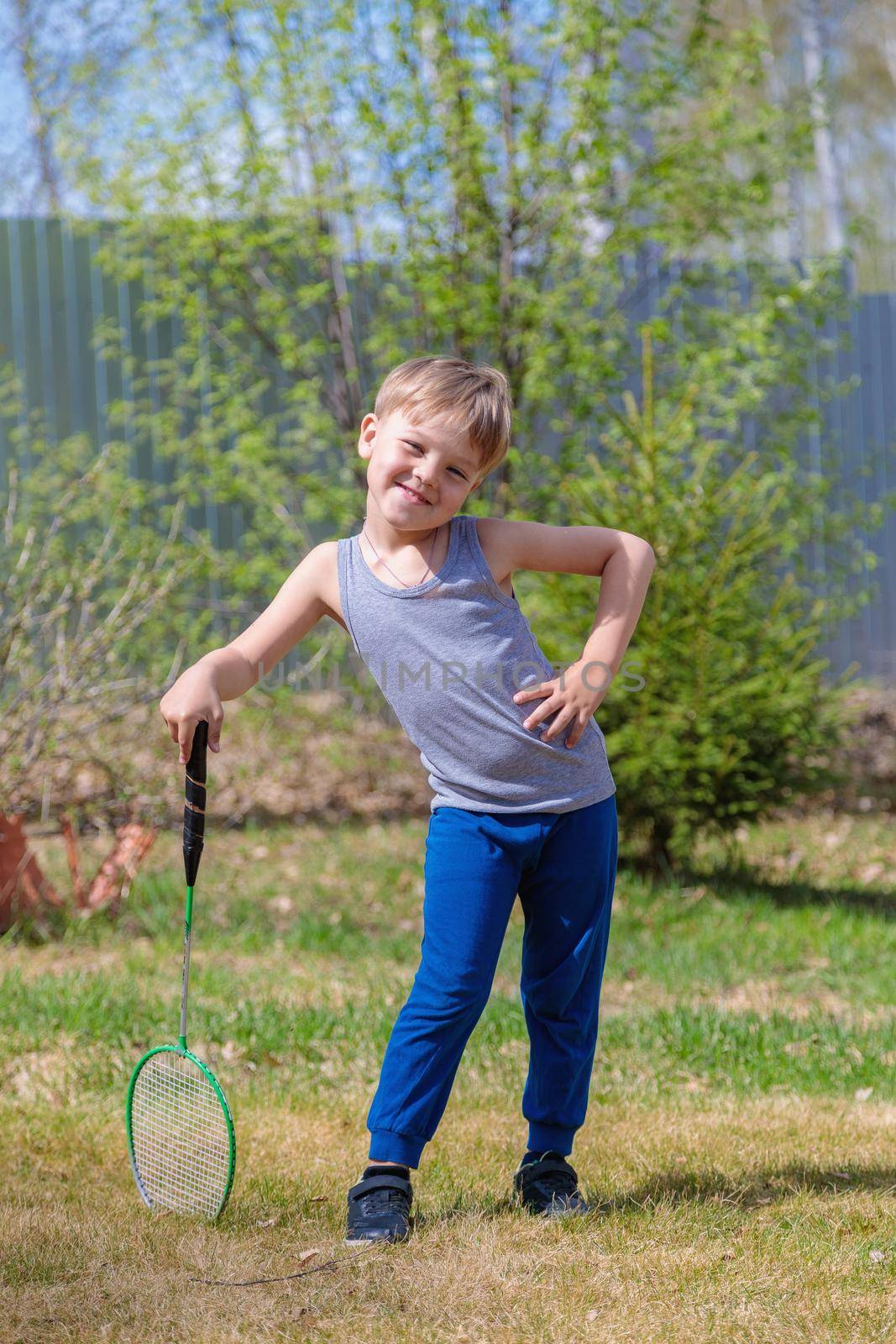 A fair-haired child plays badbinton on the lawn.