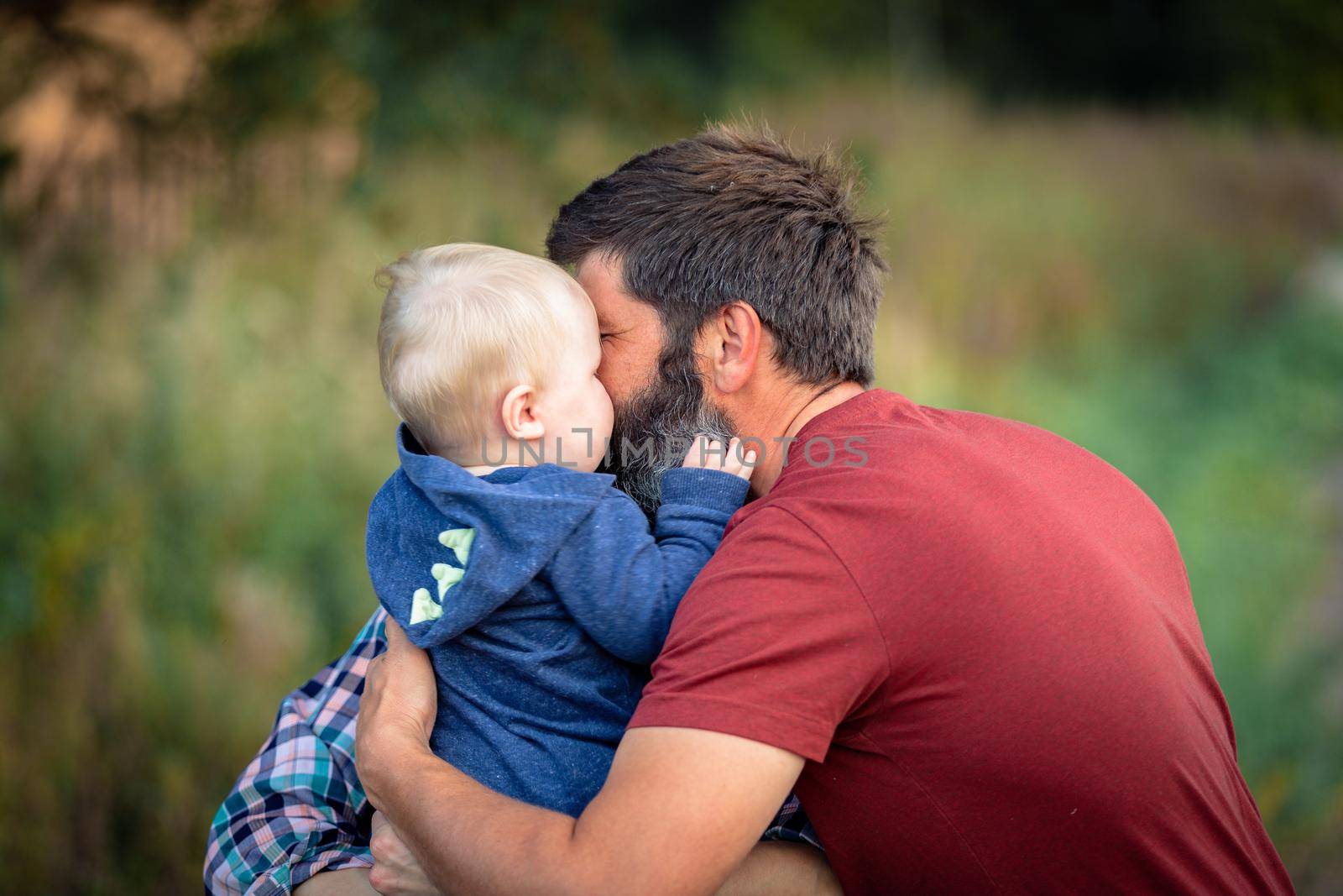 Dad plays and hugs a child walking in the park in summer. by Yurich32