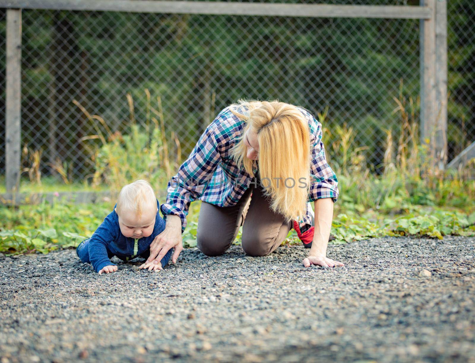 Mom plays with the child sitting on the sidewalk. Family on a walk.