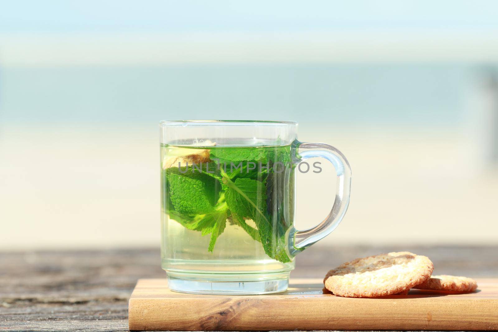 Peppermint tea with green leaves and cookies in front of a beach as a closeup