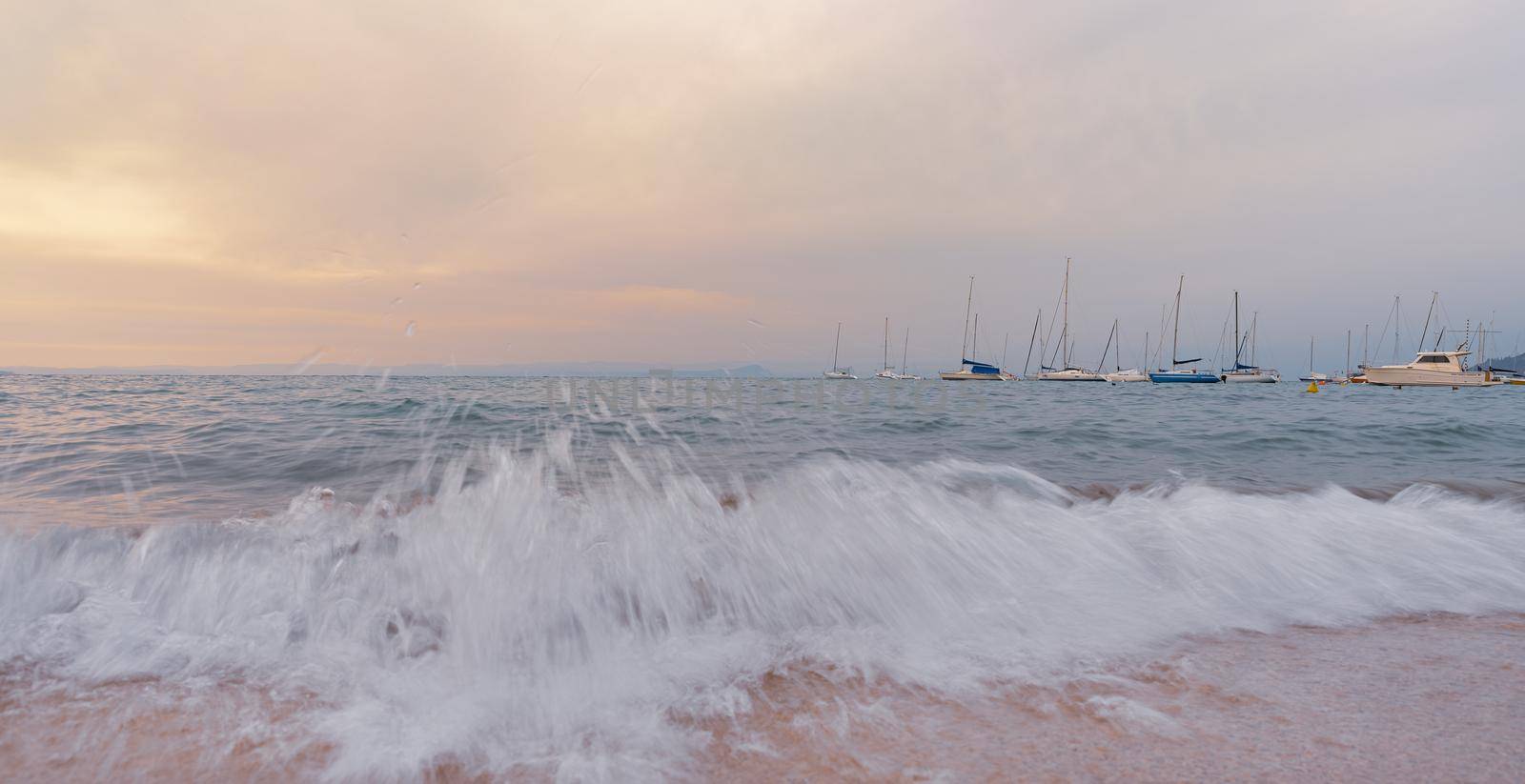 At sunset the waves break on the beach in front of boats by brambillasimone