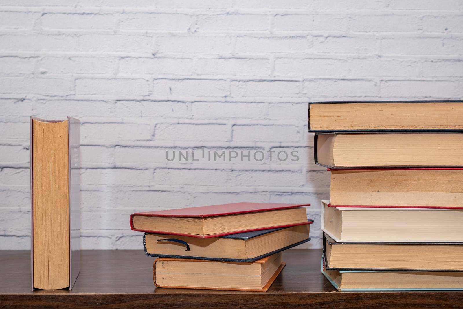 A few books of various sizes arranged on a dark wooden shelf by brambillasimone