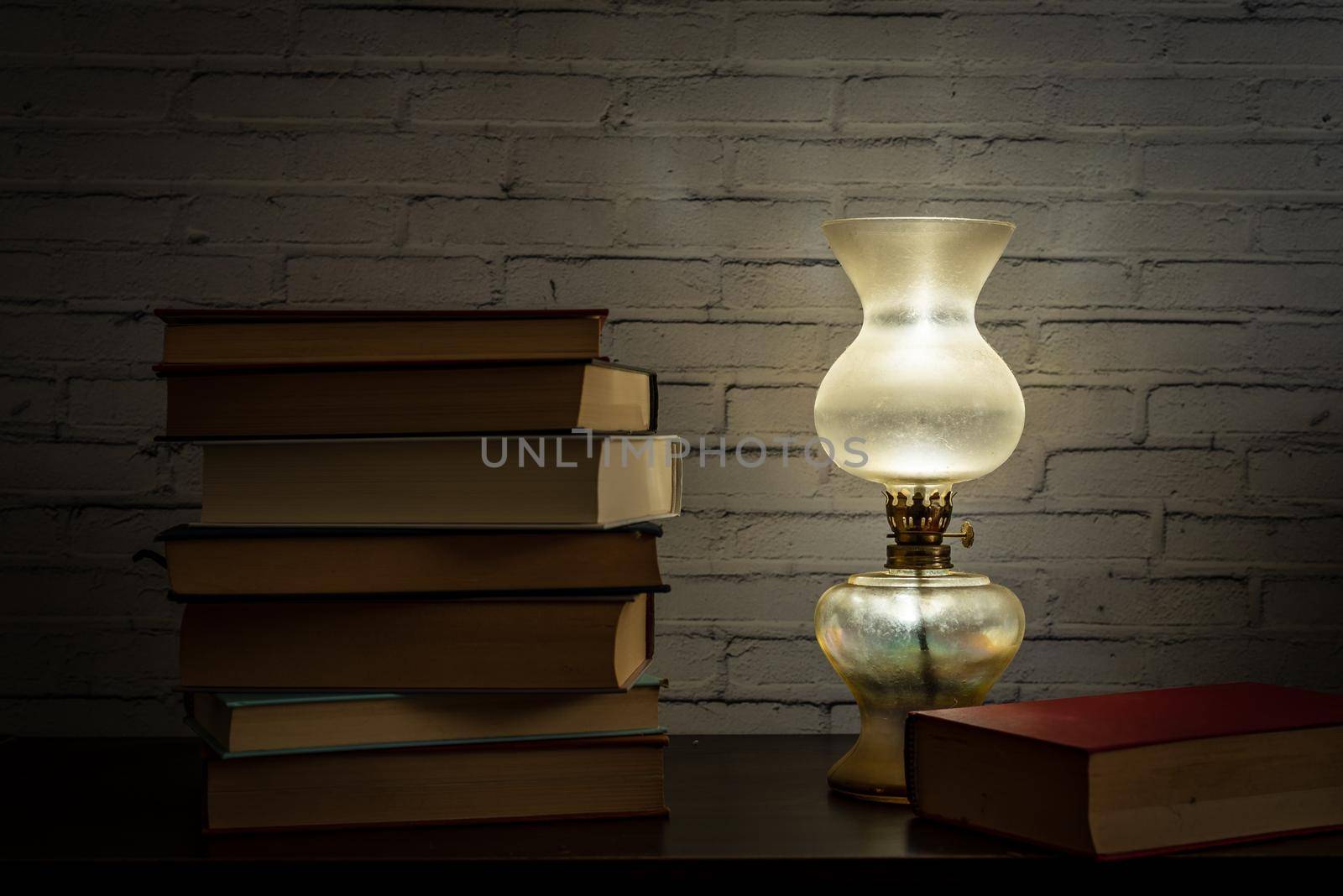 The light of an oil lamp illuminates books placed on a dark wooden surface, still life in soft light