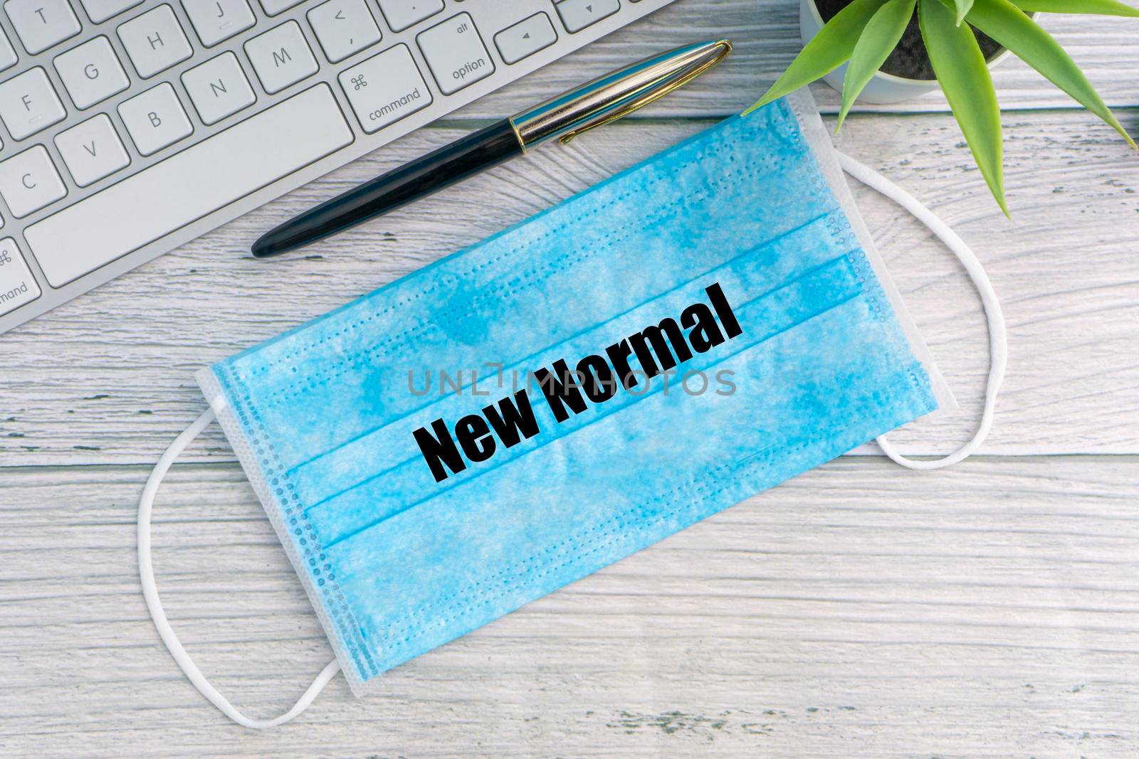 NEW NORMAL text with safety face mask, keyboard, fountain pen and decorative plant on wooden background by silverwings