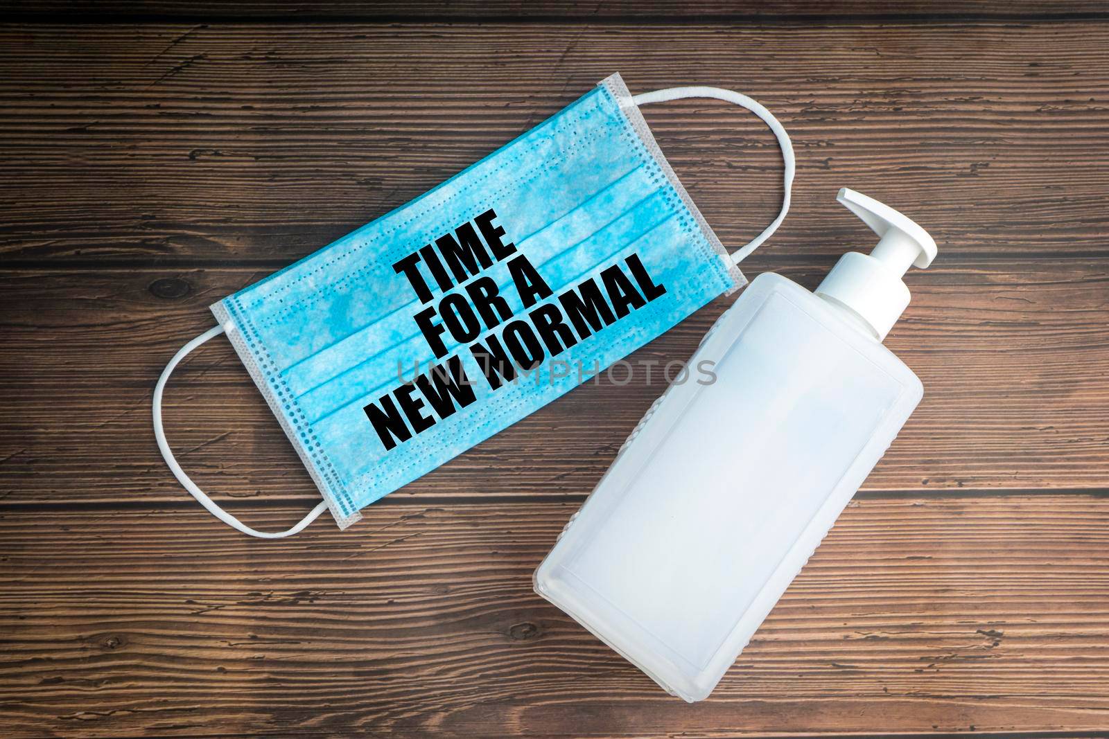 TIME FOR A NEW NORMAL text with safety face mask and hand sanitizer on wooden background by silverwings