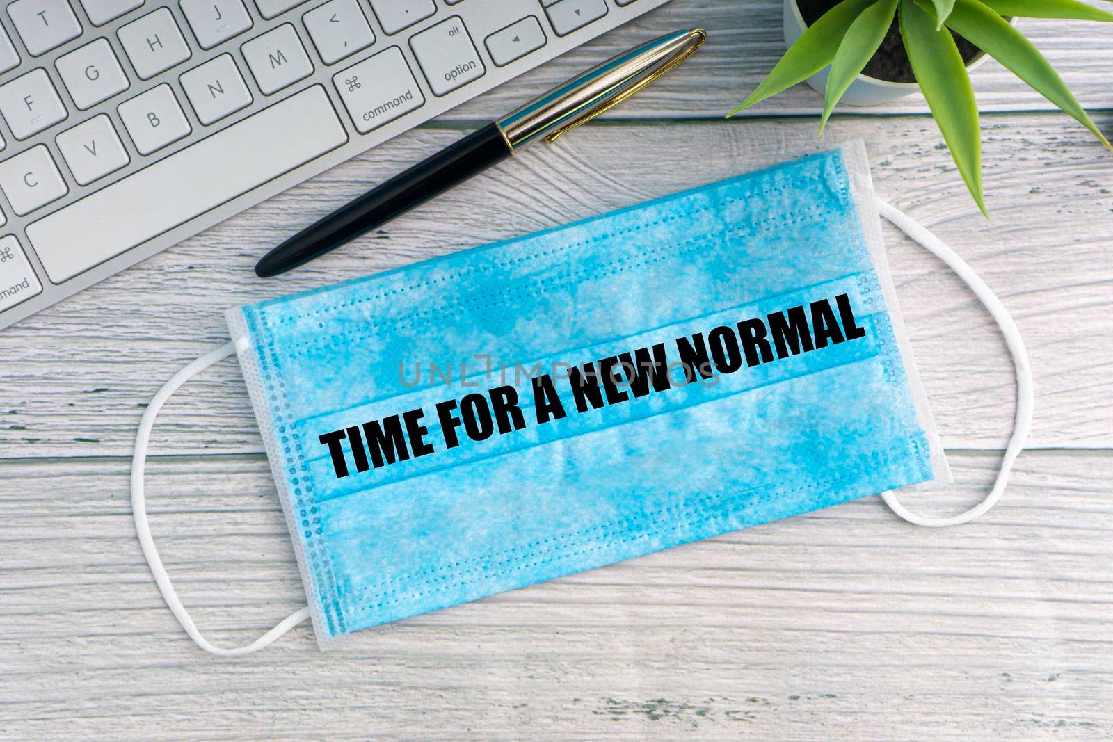 TIME FOR A NEW NORMAL text with safety face mask, keyboard, fountain pen and decorative plant on wooden background by silverwings