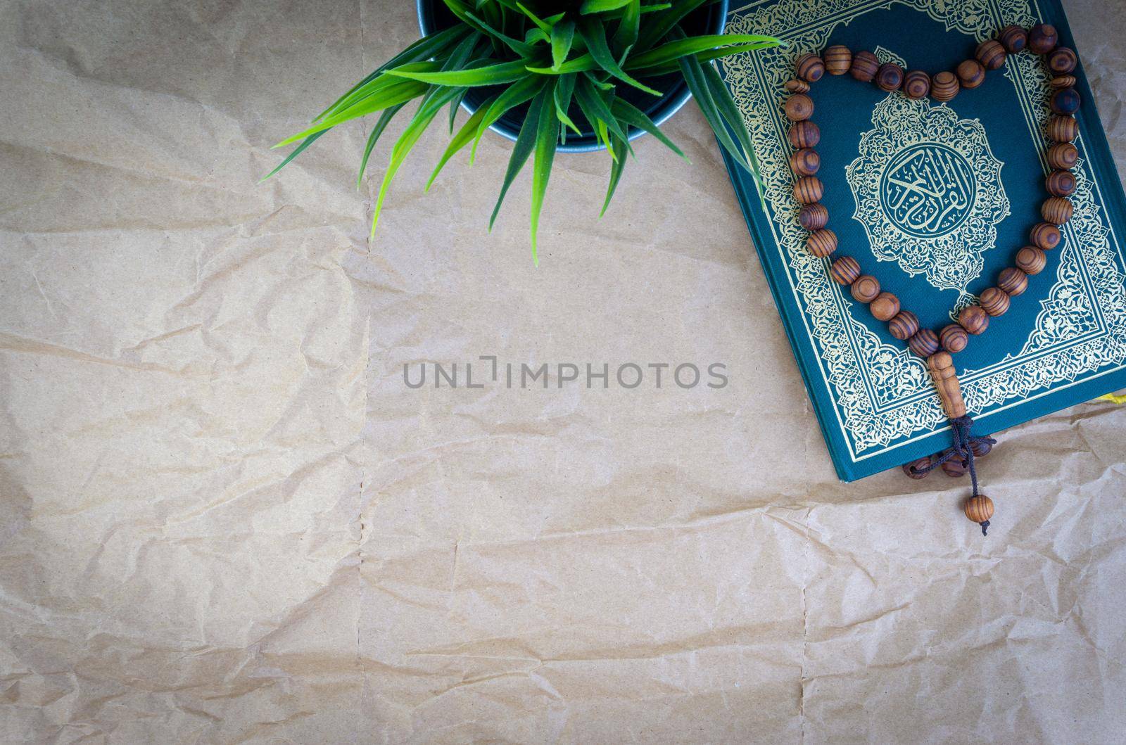 Flat lay Holy Quran with arabic calligraphy meaning of Al Quran and tasbih or rosary beads over wooden paper background. Selective focus and crop fragment