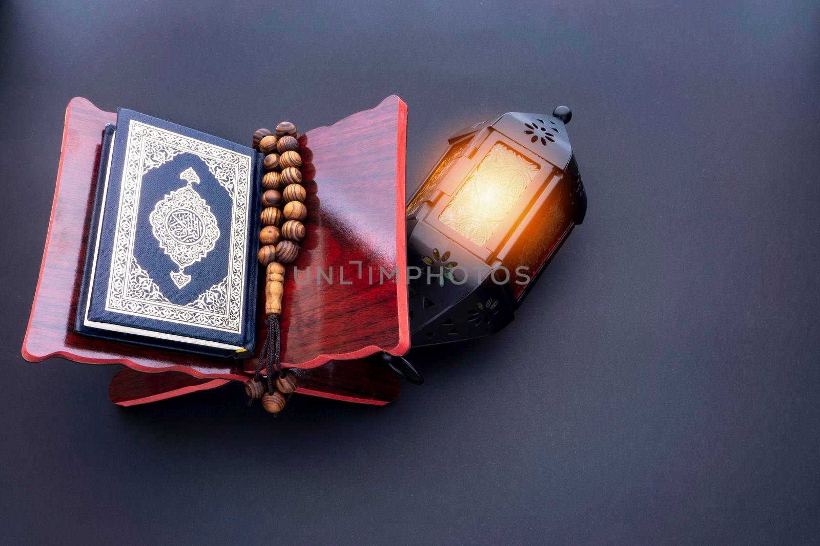 Holy Al Quran with written arabic calligraphy meaning of Al Quran, lantern lamp and rosary beads or tasbih on black background. by silverwings