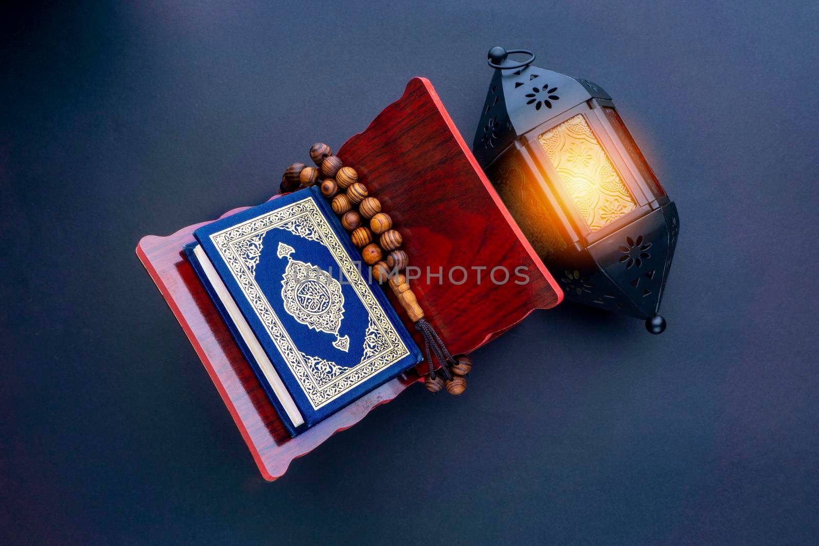 Holy Al Quran with written arabic calligraphy meaning of Al Quran, lantern lamp and rosary beads or tasbih on black background. by silverwings