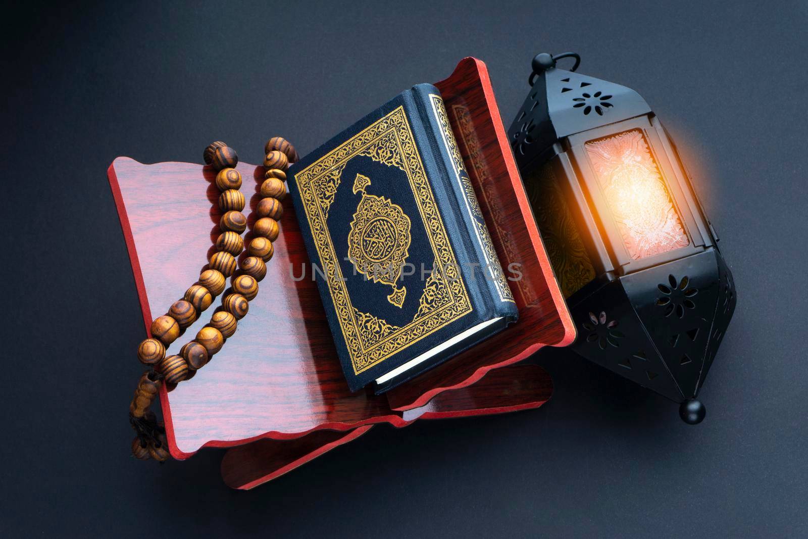 Holy Al Quran with written arabic calligraphy meaning of Al Quran, lantern lamp and rosary beads or tasbih on black background. by silverwings