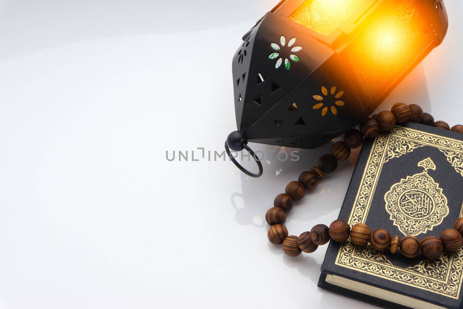 Holy Al Quran with written arabic calligraphy meaning of Al Quran, lantern and rosary beads or tasbih on white background by silverwings