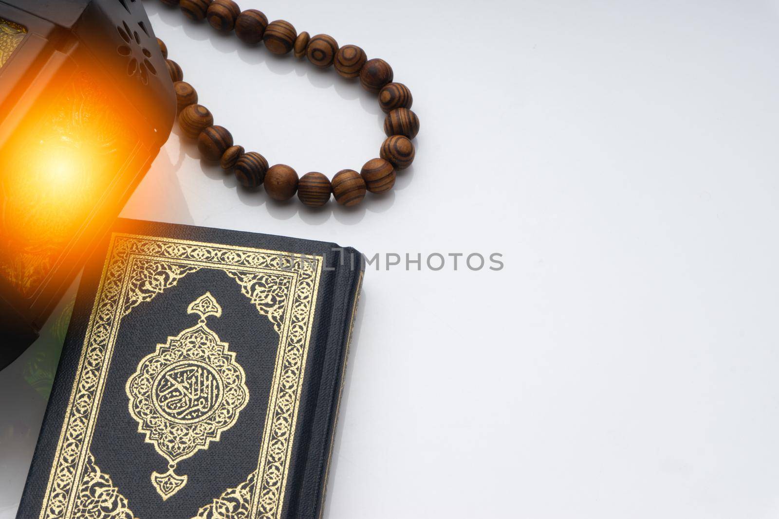 Holy Al Quran with written arabic calligraphy meaning of Al Quran, lantern and rosary beads or tasbih on white background. Copy space and crop fragment