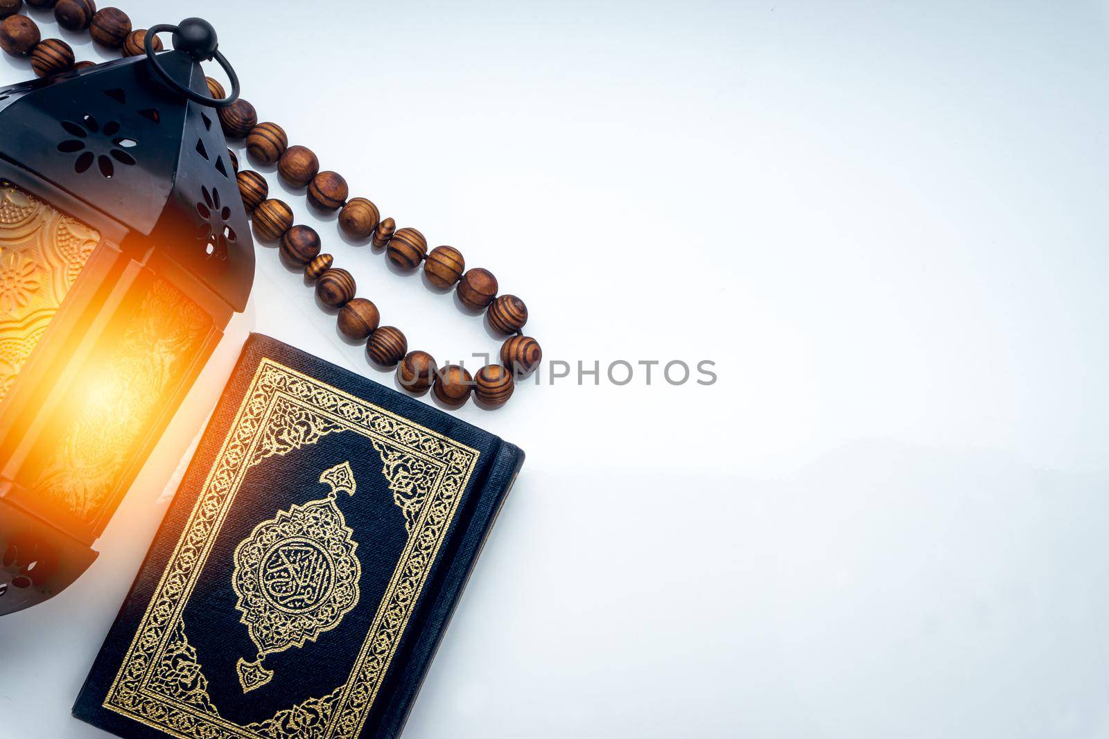 Holy Al Quran with written arabic calligraphy meaning of Al Quran, lantern and rosary beads or tasbih on white background. Copy space and crop fragment