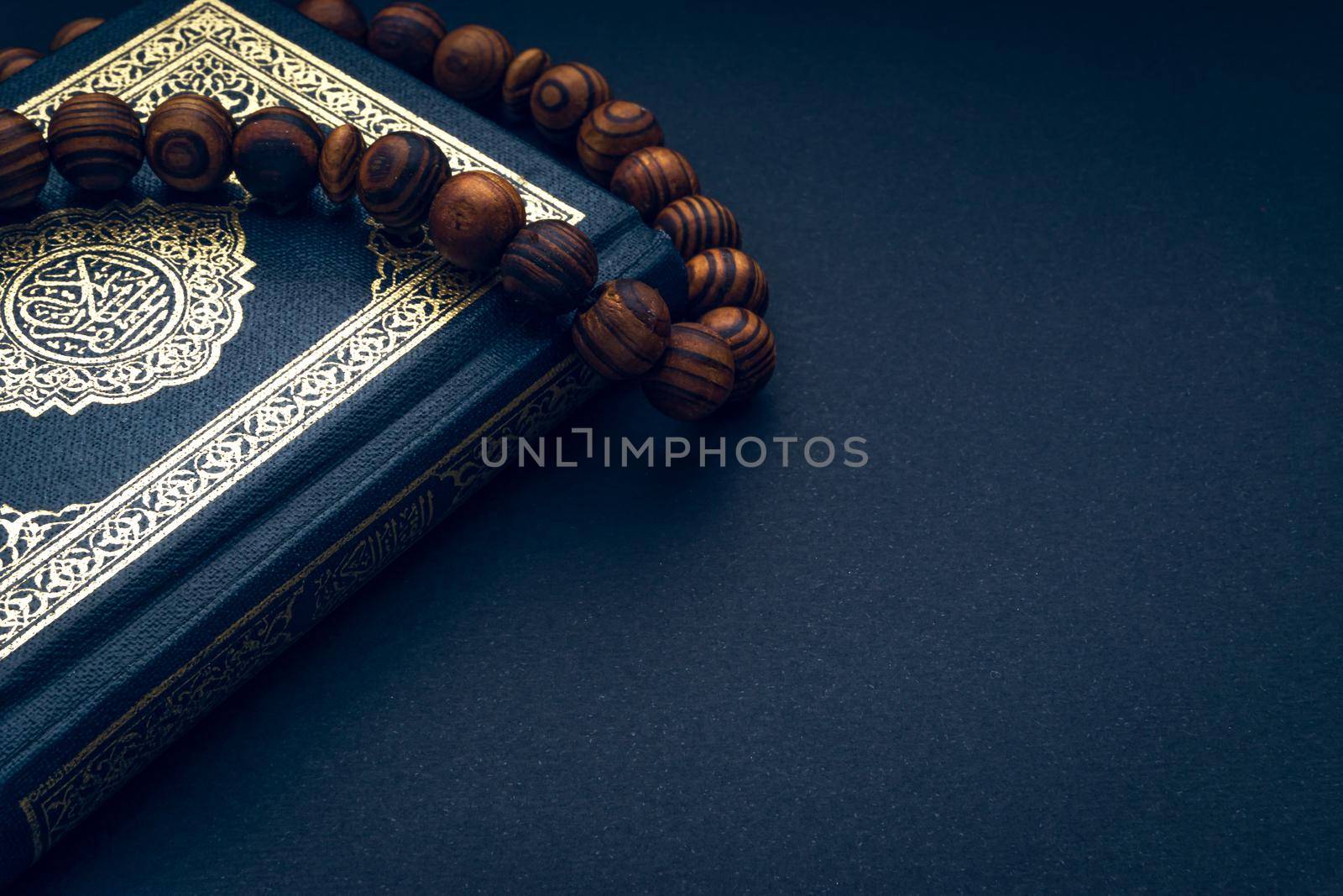 Holy Al Quran with written arabic calligraphy meaning of Al Quran and rosary beads or tasbih on black background by silverwings