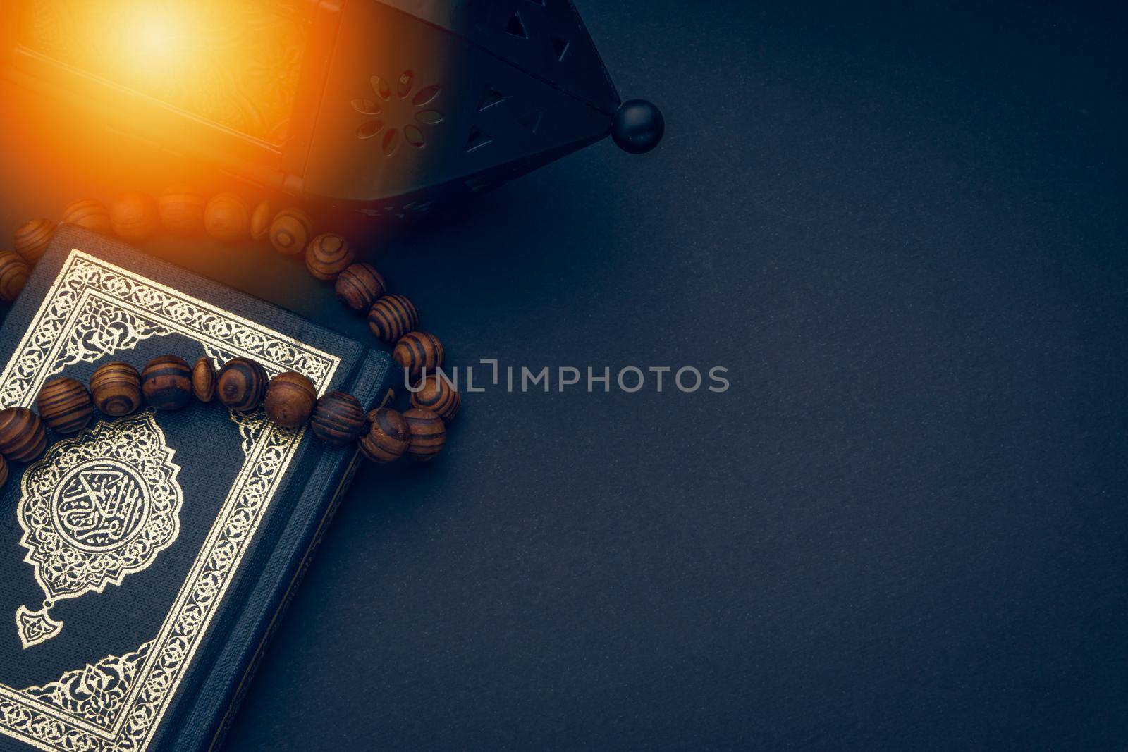 Holy Al Quran with written arabic calligraphy meaning of Al Quran, lantern and rosary beads or tasbih on black background. Copy space and crop fragment