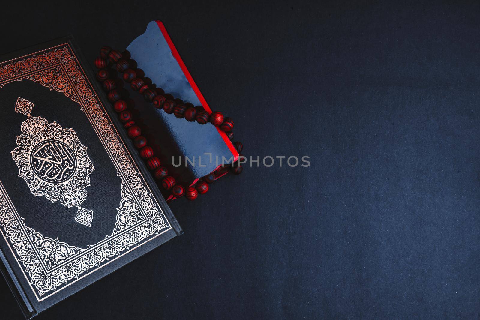 Holy Al Quran with written arabic calligraphy meaning of Al Quran and tasbih or rosary beads on black background by silverwings
