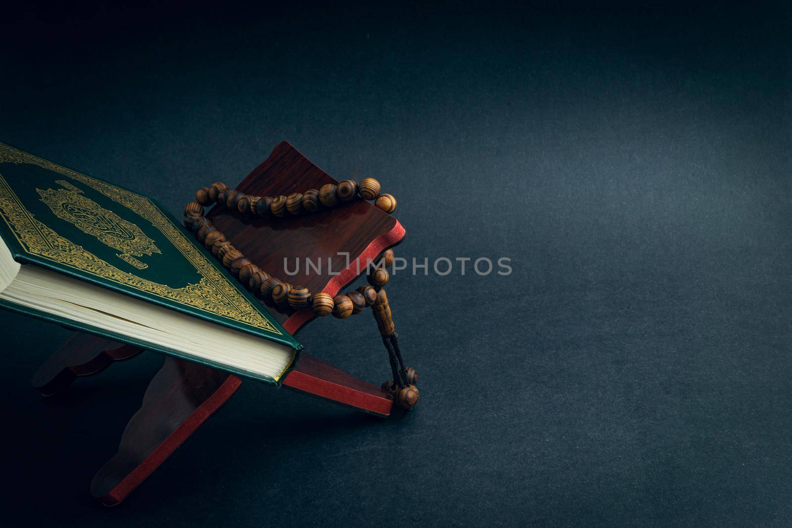 Holy Al Quran with written arabic calligraphy meaning of Al Quran and tasbih or rosary beads on black background by silverwings