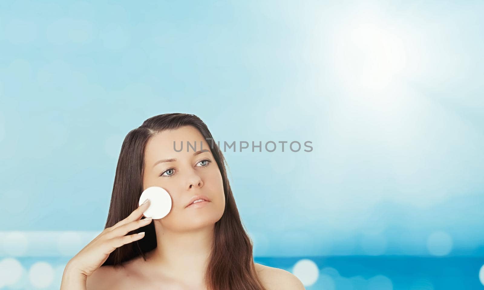 Skincare and sun protection in summer. Portrait of a beautiful young suntanned woman, blue sea and sky on background, beauty, wellness and travel concept.