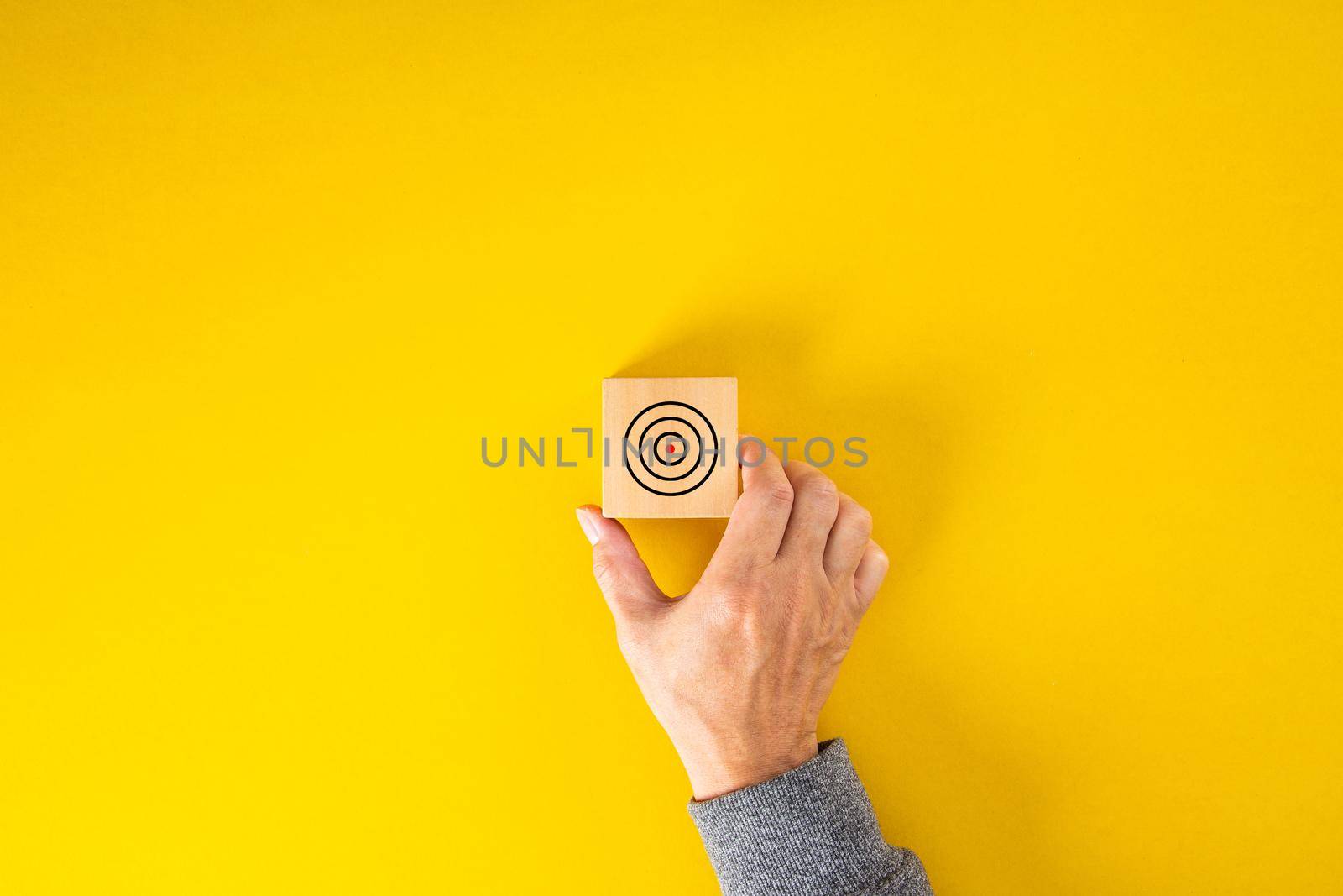 businessman hand put square block with aim at concentric circles of marketing target on yellow background