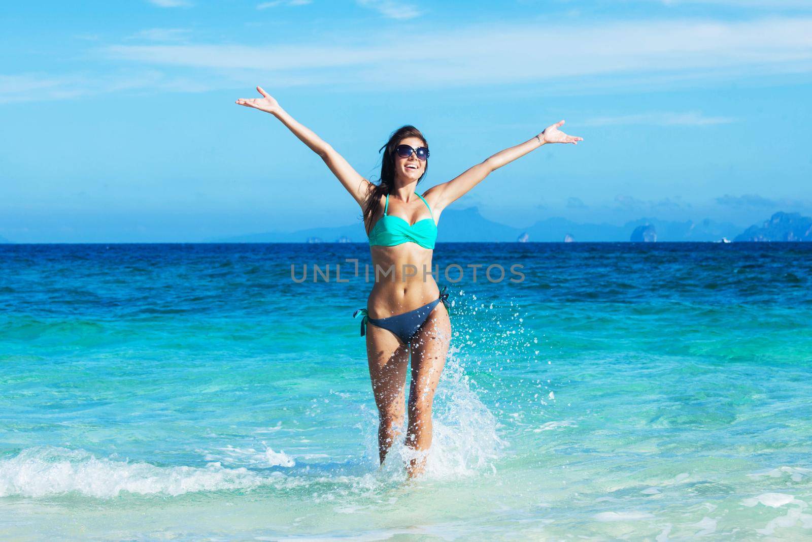 Beautiful happy woman in splashing in the sea with raised arms