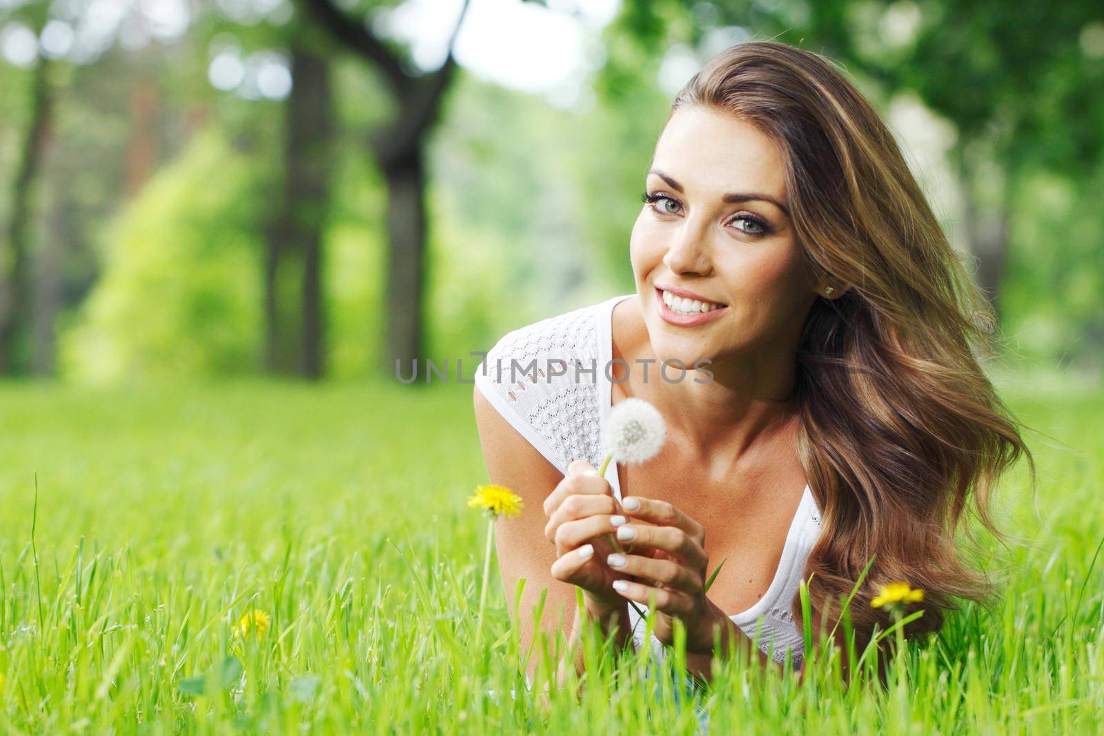 Cute smiling woman lay in the park with dandelion flowers