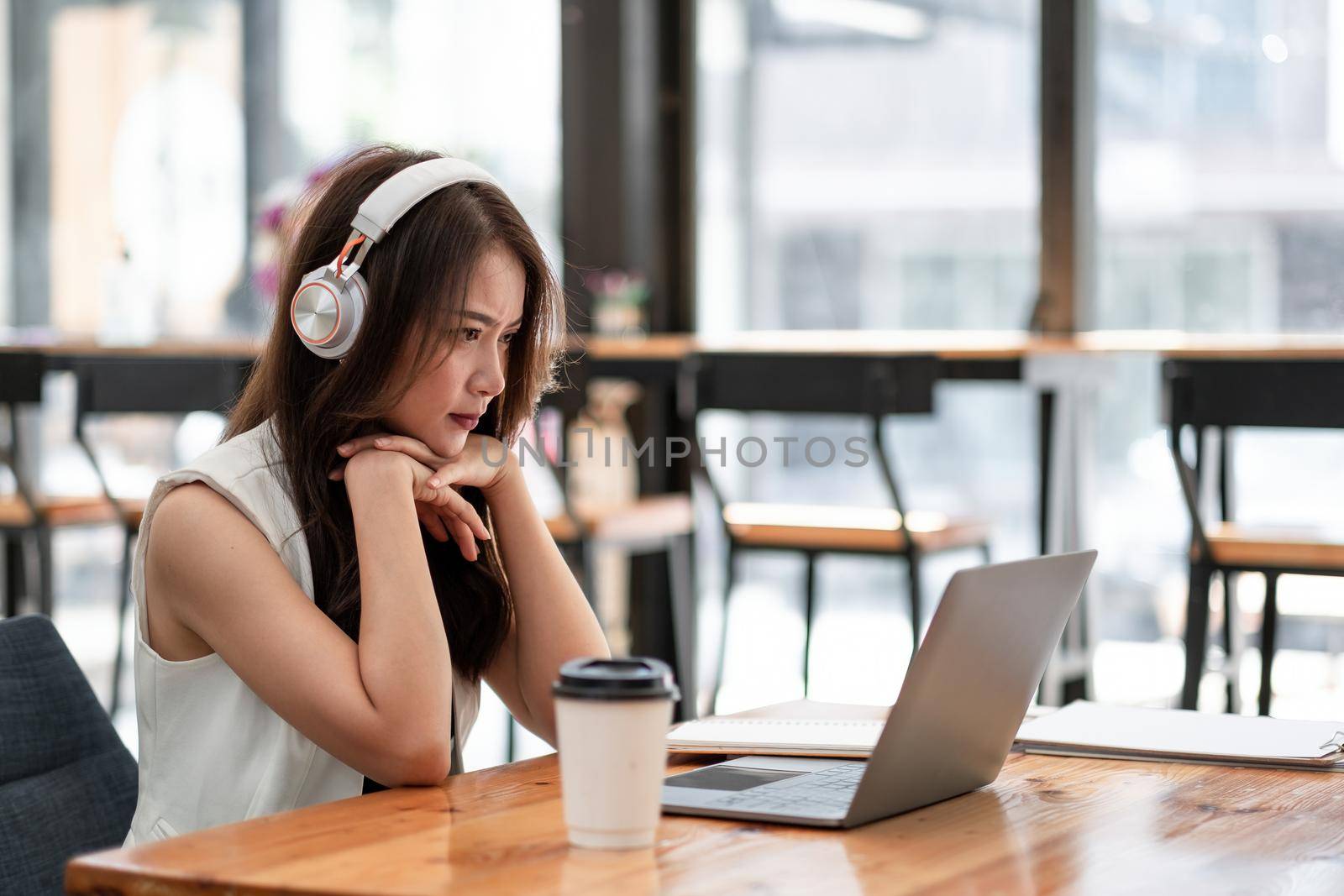 Concentrated young asian female wearing headphone look at laptop for online study, attractive female student learning language, watching online webinar, e-learning education concept