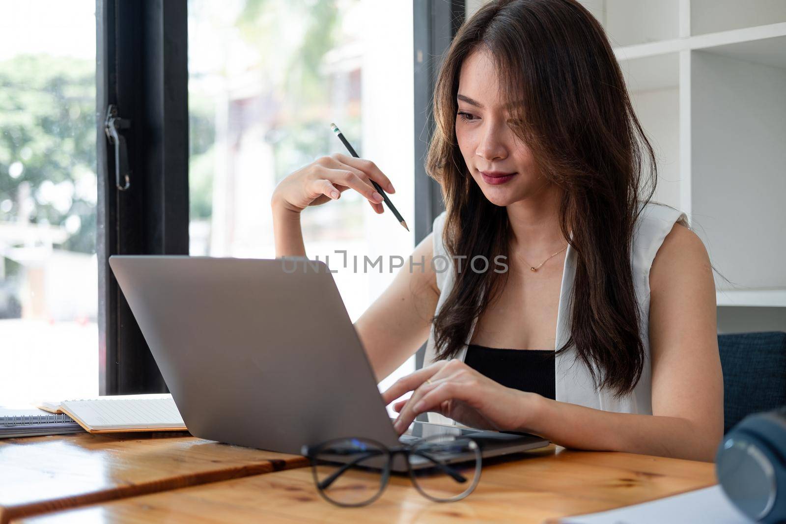 Beautiful young asian woman working on laptop computer while taking note at home office by nateemee