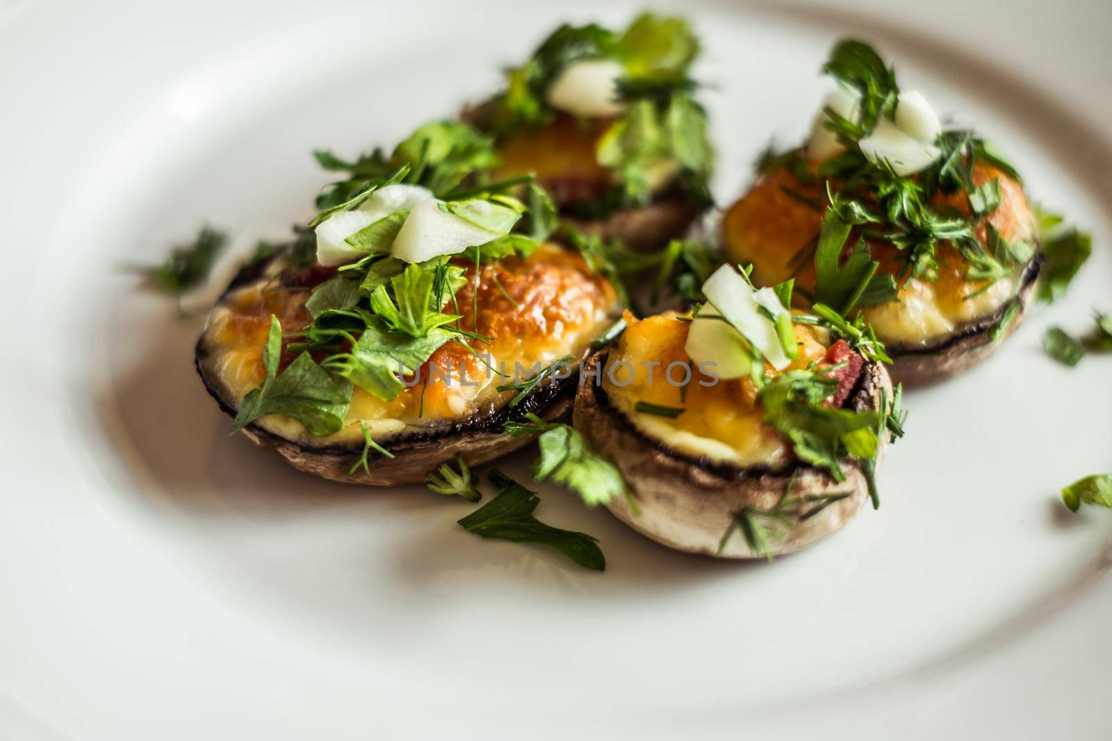 Baked champignons mushrooms, filled with cheese, parsley and roasted garlic on white plate