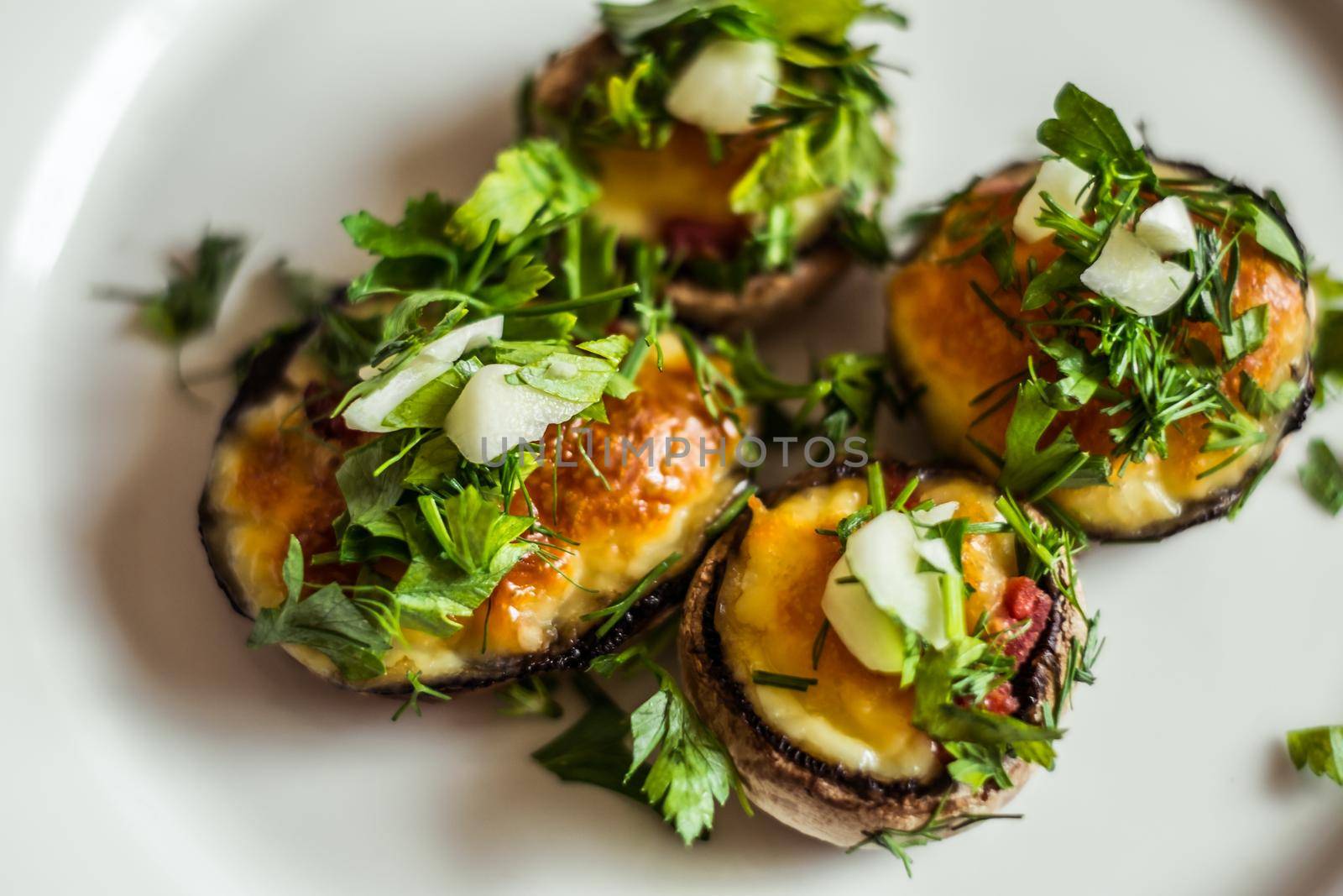 Baked champignons mushrooms, filled with cheese, parsley and roasted garlic on white plate