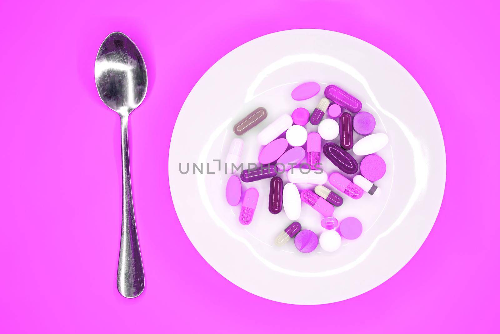 white plate with pills and spoon on turquoise background by Roberto