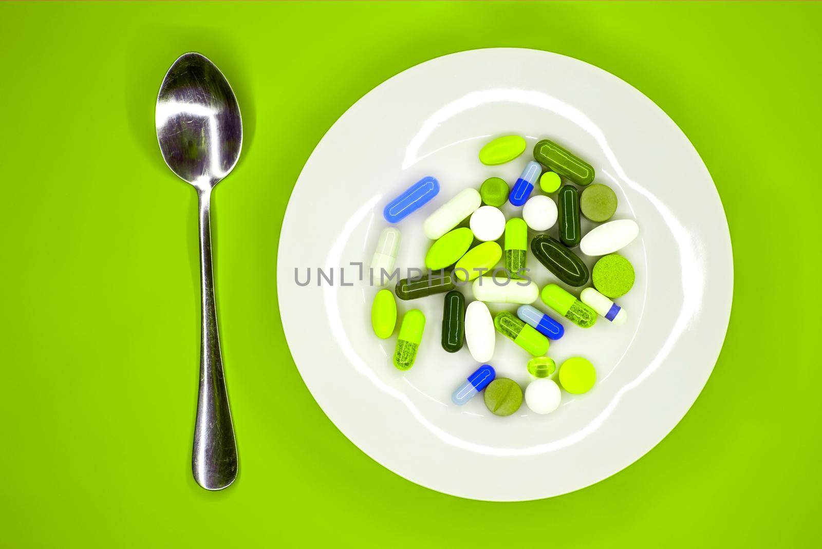 white plate with pills and spoon on turquoise background