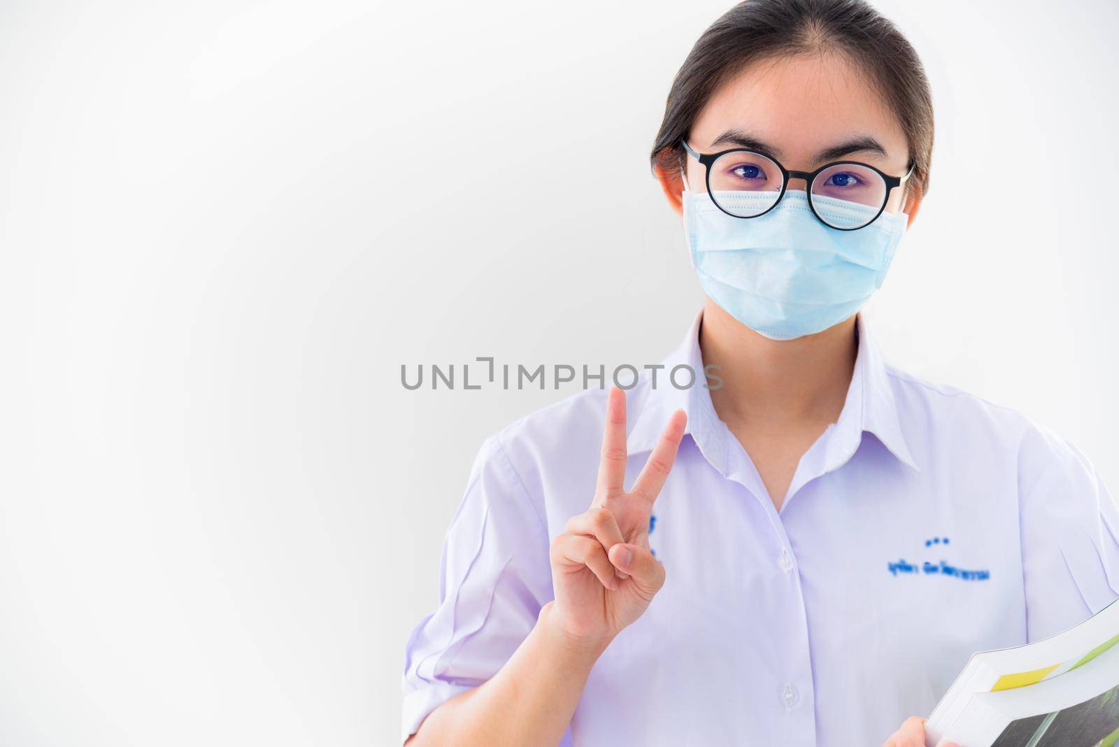 Student Asian young woman wears a mask to protect Coronavirus spread, Thai girl to encourage show two fingers symbol to fight and strong on white background healthy care from Covid 19 virus outbreak