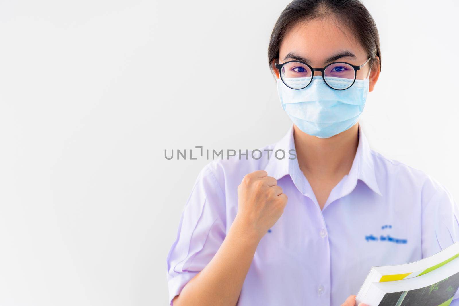 Student Asian young woman wears a mask to protect Coronavirus spread, Thai girl to encourage show fist symbol to fight and strong on white background healthy care from Covid 19 virus outbreak concept