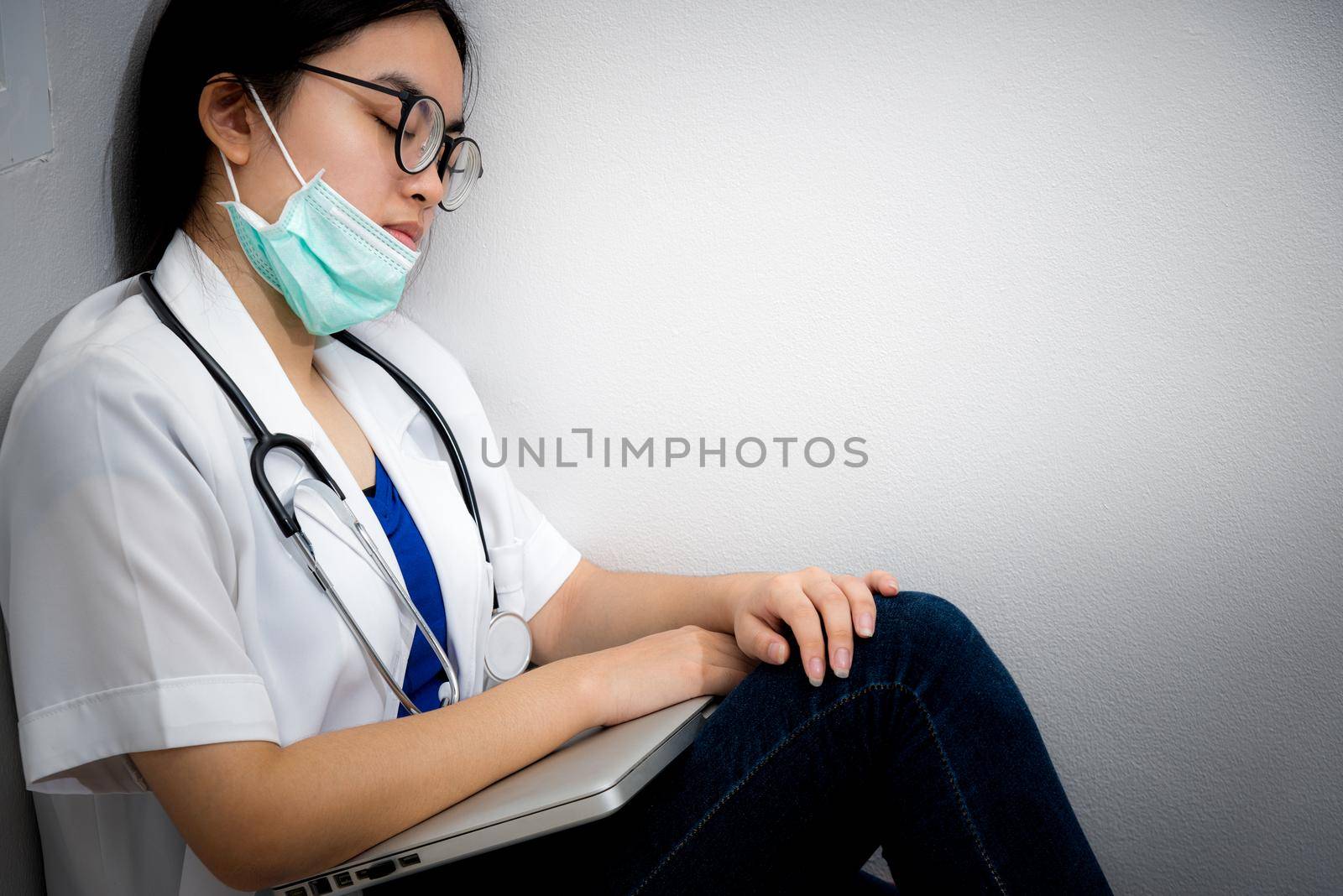 Asian young woman doctor wear mask to safety Coronavirus sit on the corner floor sleeping with exhaustion from overwork concept take care yourself is to help physician stop the epidemic Covid-19 virus