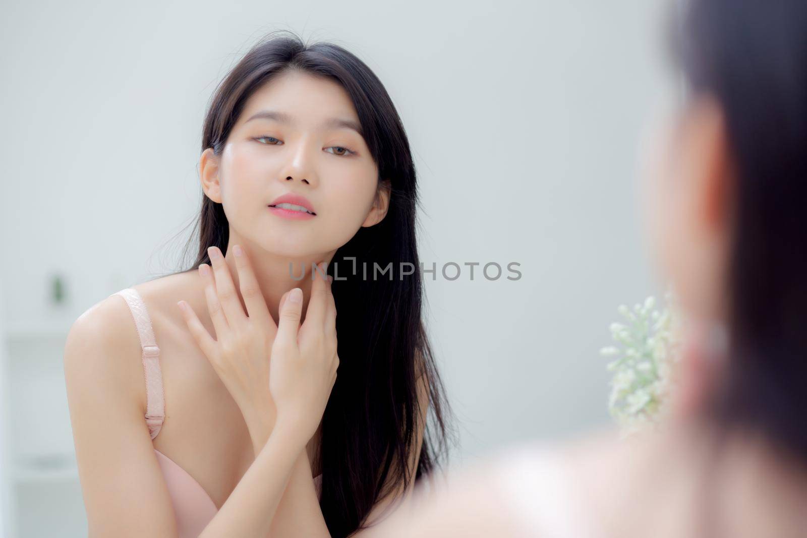 Beautiful sexy young asian woman looking mirror applying cream on neck and message, beauty girl applying body lotion skin care for health and soft hydration, treatment and cosmetic with moisturizer.