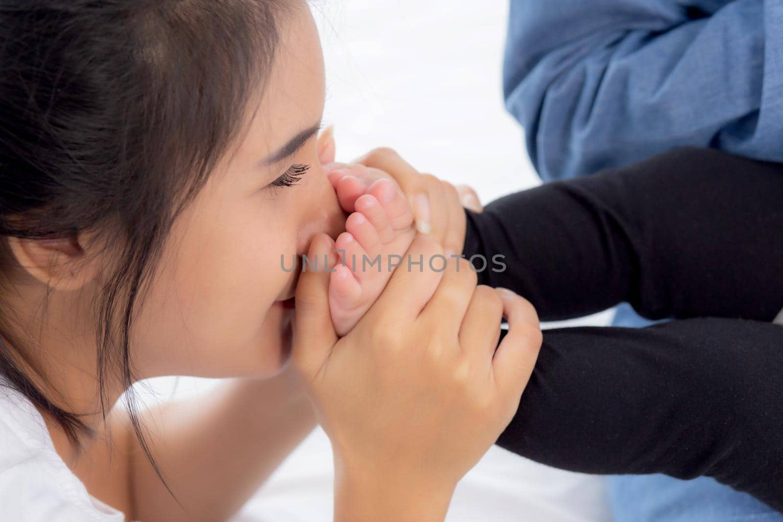 Young asian mother kiss foot of little baby girl on bed in bedroom at home, mom and newborn with relationship and bonding together, motherhood with love and care child with happy, family concept.