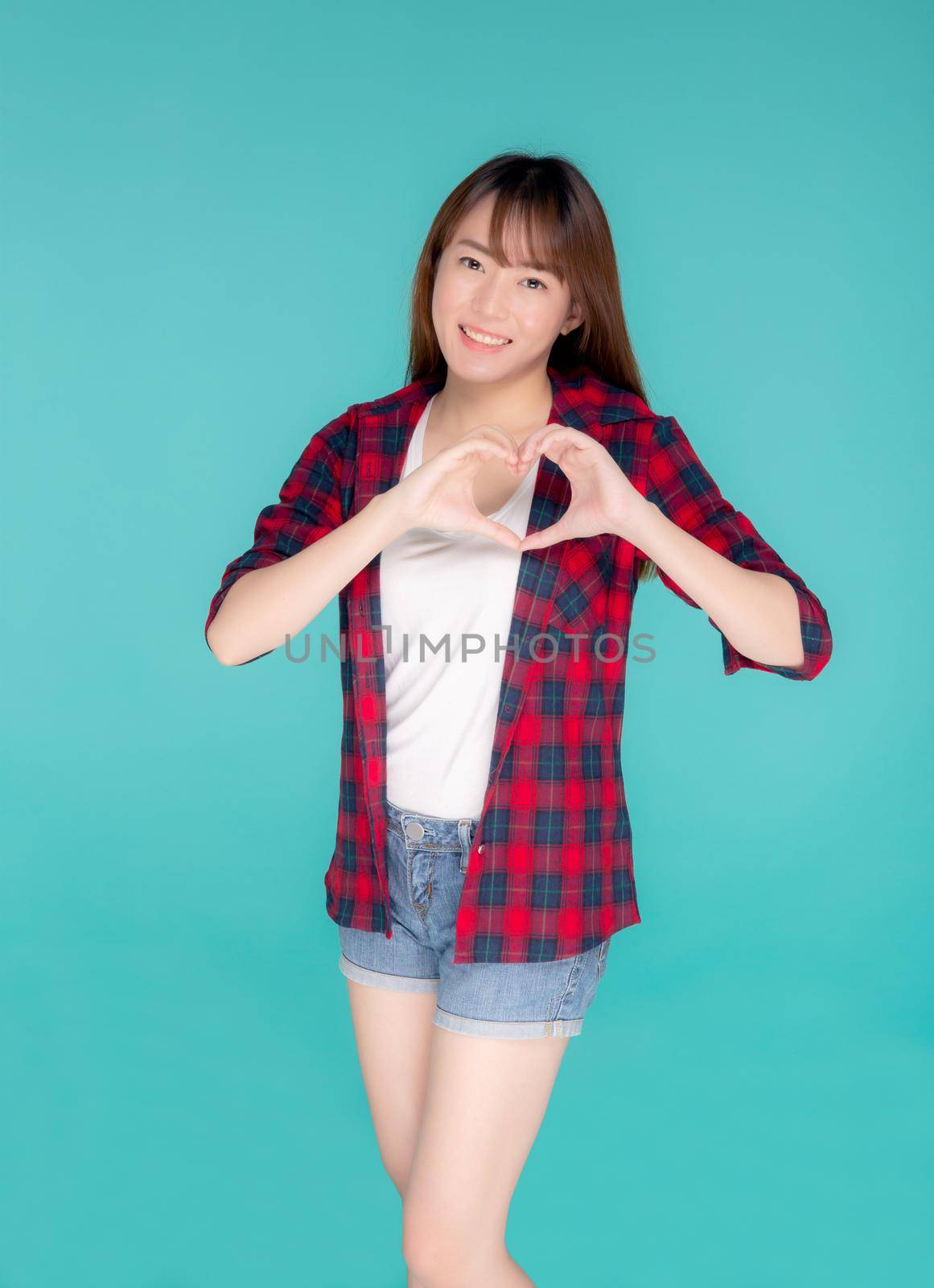 Beautiful happy young asian woman wear travel summer gesture heart shape with hand having confident isolated on blue background, asia teenager girl expression with cheerful and fun while trip. by nnudoo