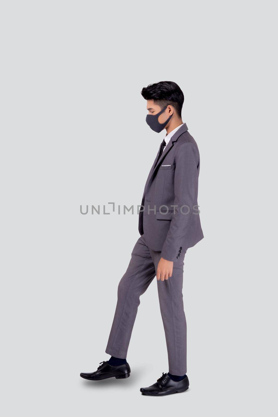 Portrait young asian businessman in suit wearing face mask walk step for protective covid-19 isolated on white background, business man and healthcare, quarantine for pandemic coronavirus, new normal. by nnudoo